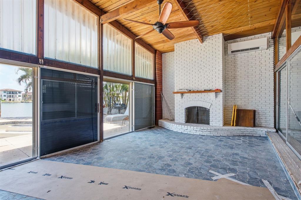 A sunroom features a white brick fireplace, wood-paneled ceiling, and sliding glass doors overlooking water — 31 DOLPHIN DRIVE, TREASURE ISLAND, FL