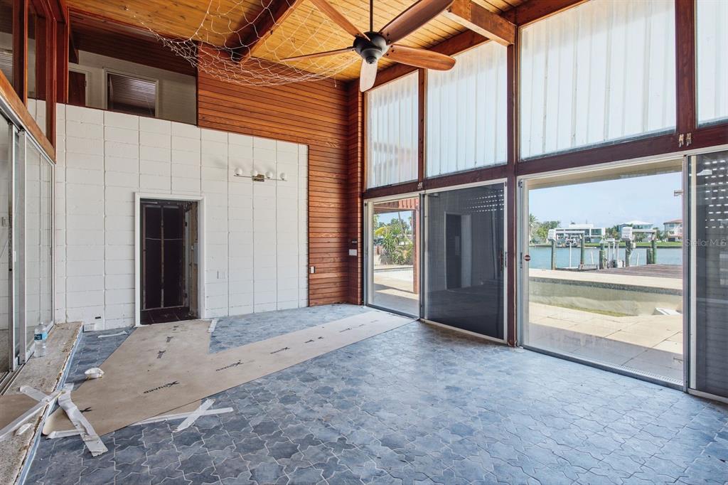 A sunroom with wood-paneled walls, a ceiling fan, and sliding glass doors overlooking a canal — 31 DOLPHIN DRIVE, TREASURE ISLAND, FL