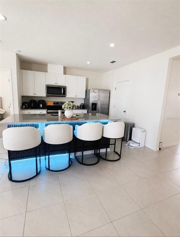 A modern kitchen features white cabinetry, stainless steel appliances, and a breakfast bar with stools — 452 TAYLOR GROVES DRIVE, LAKE WALES, FL