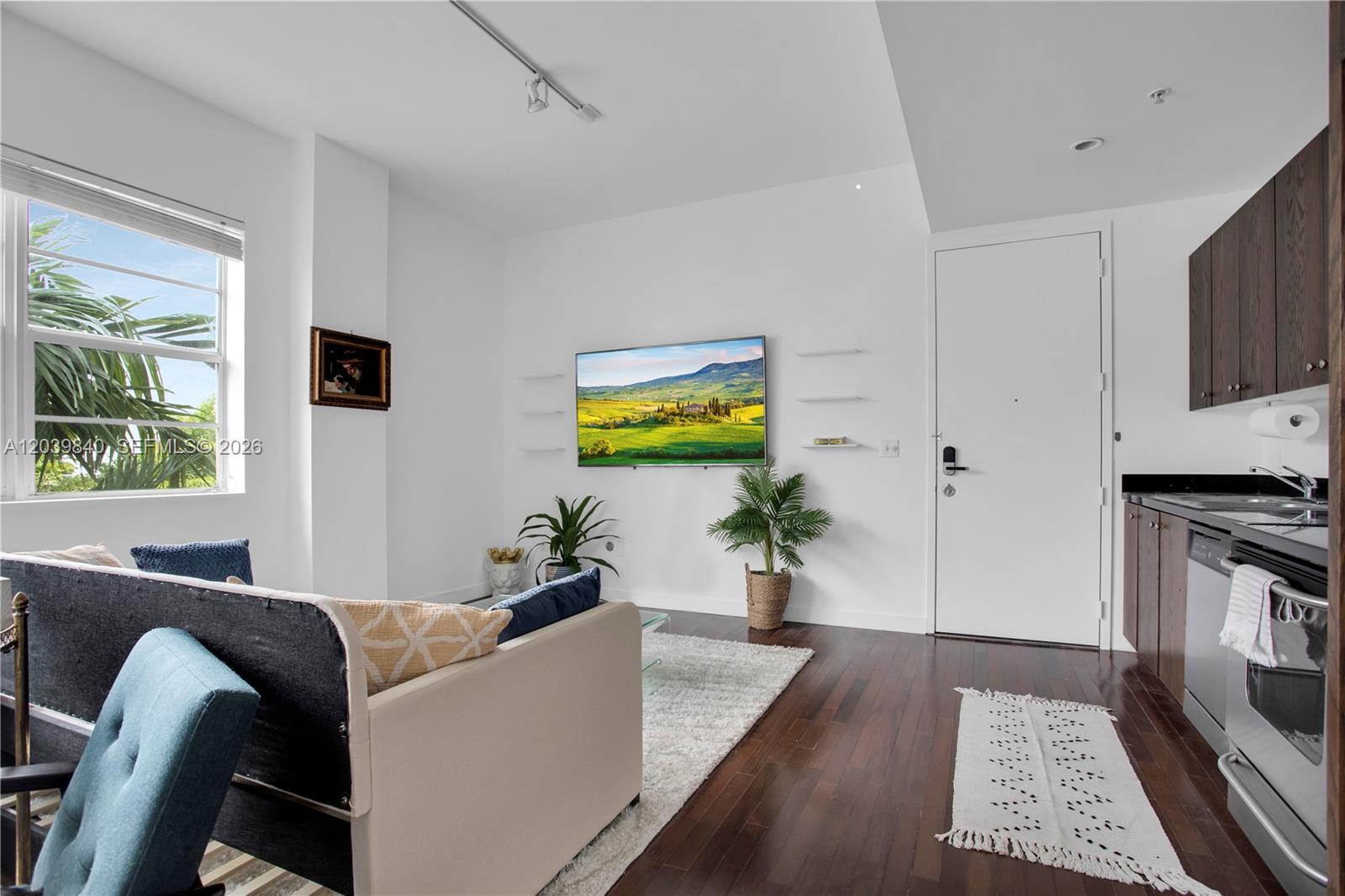 A living room with dark wood floors, a wall-mounted television, and an adjacent kitchen area — 935 Euclid Ave # 8, Miami Beach FL 33139, MIAMI BEACH, FL