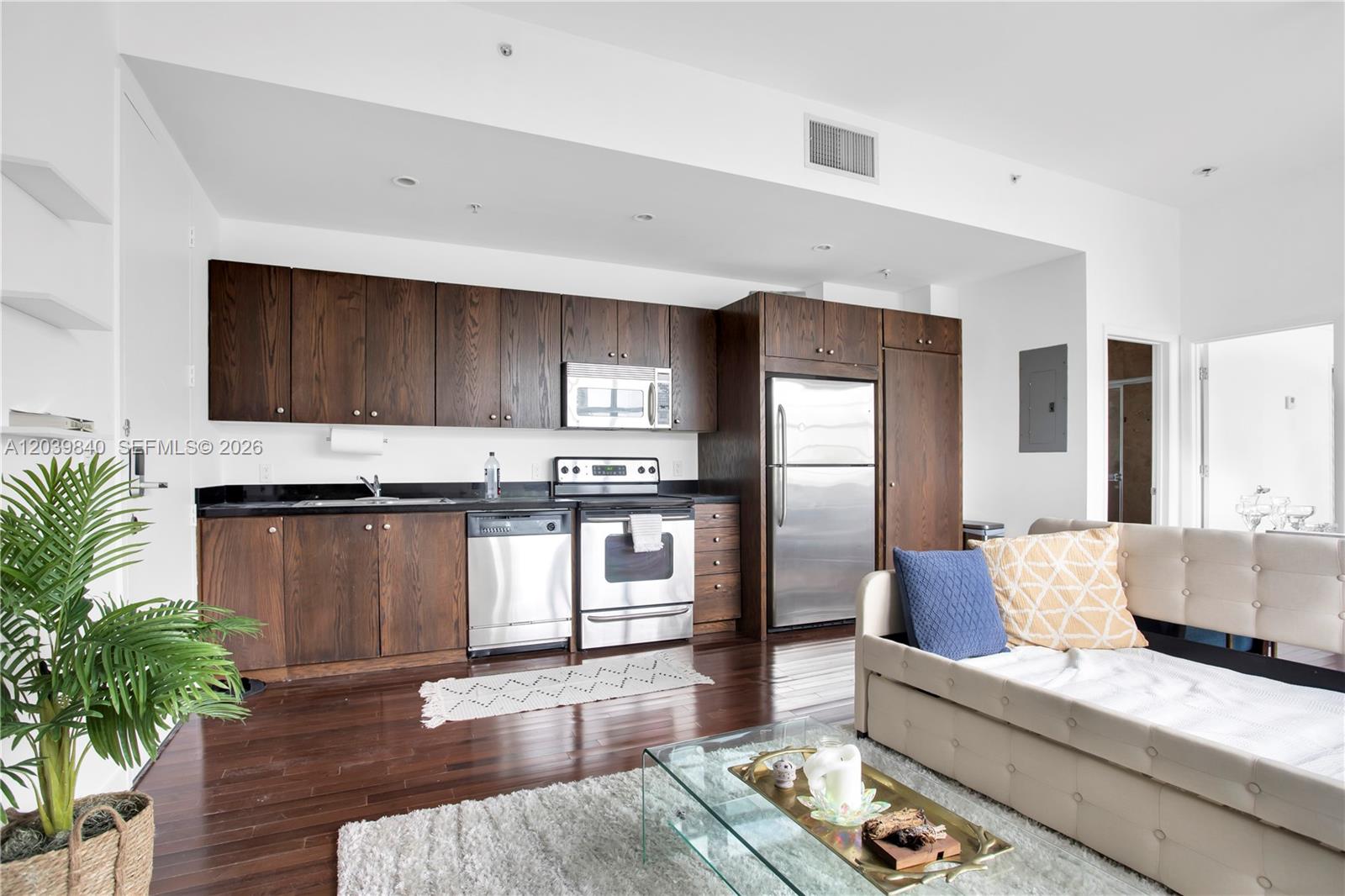 A kitchen with dark wood cabinets and stainless steel appliances sits beside a living area — 935 Euclid Ave # 8, Miami Beach FL 33139, MIAMI BEACH, FL
