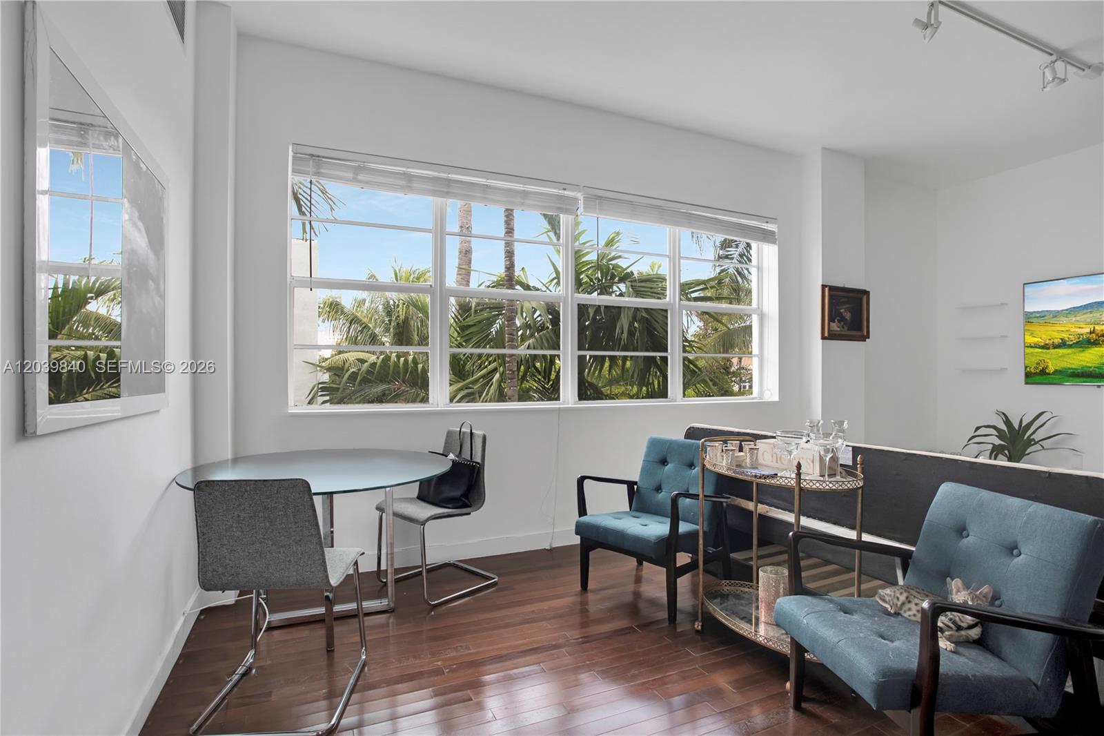 A living and dining area features hardwood floors, large windows with palm views, and blue chairs — 935 Euclid Ave # 8, Miami Beach FL 33139, MIAMI BEACH, FL