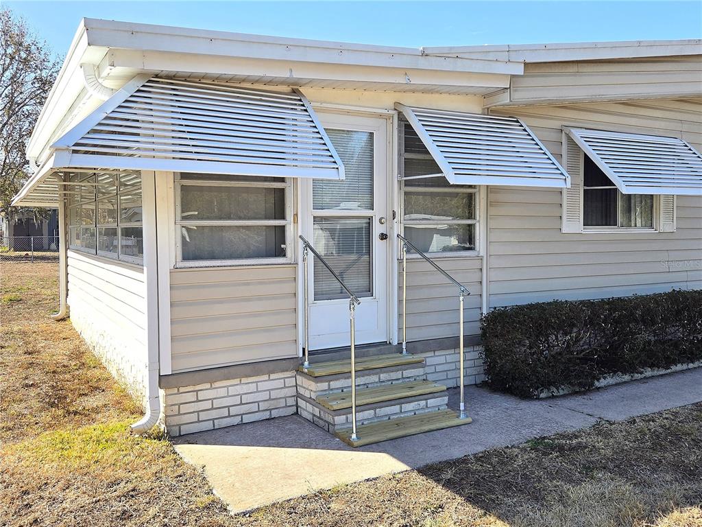 The exterior of a mobile home features a white door, metal awnings, and wooden steps — 480 NE 64TH AVENUE, OCALA, FL