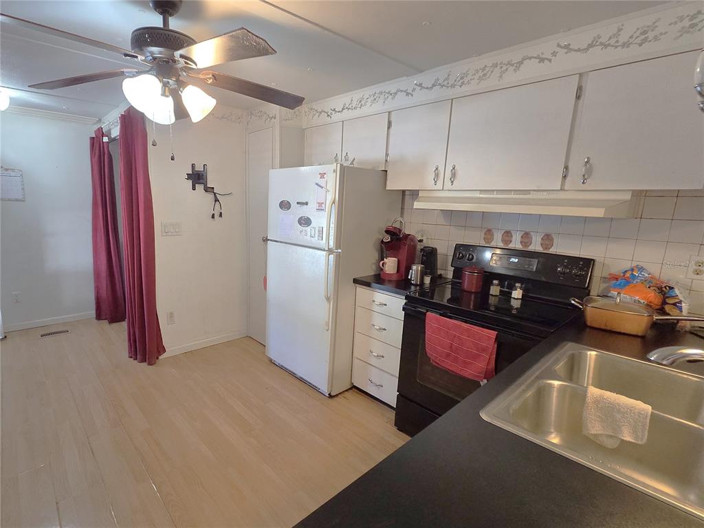 A kitchen features white cabinets, a white refrigerator, a black stove, and light wood flooring — 480 NE 64TH AVENUE, OCALA, FL