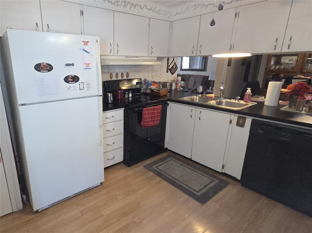 A kitchen features white cabinets, black appliances, a double sink, and light wood-look flooring — 480 NE 64TH AVENUE, OCALA, FL