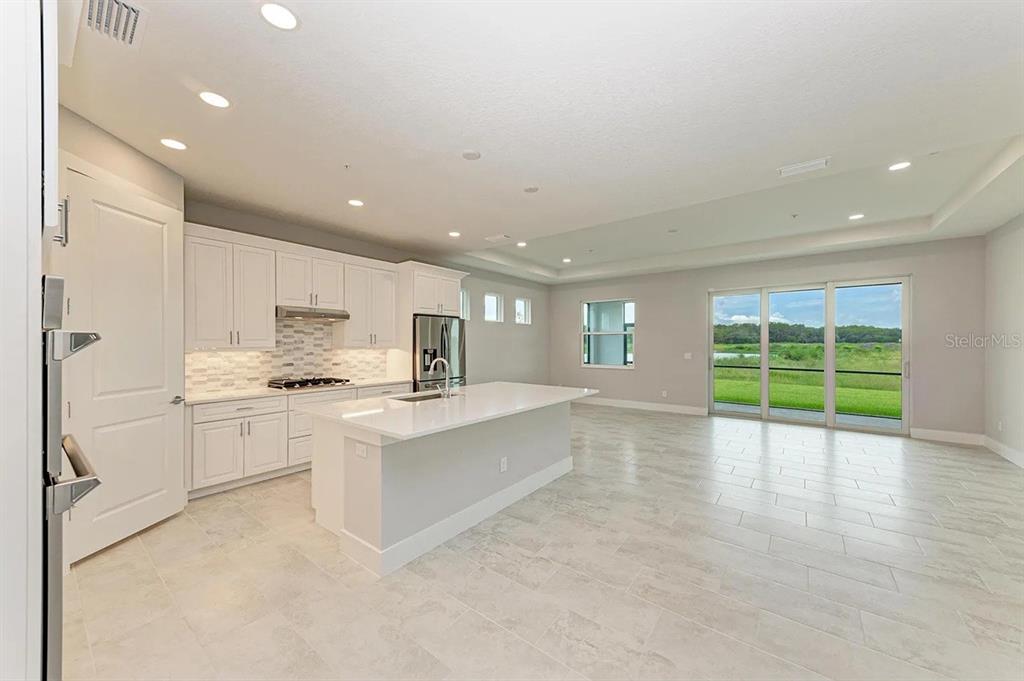 A modern kitchen with white cabinets, a central island, and sliding doors to a backyard — 10016 REMBRANDT WAY UNIT 102, BRADENTON, FL