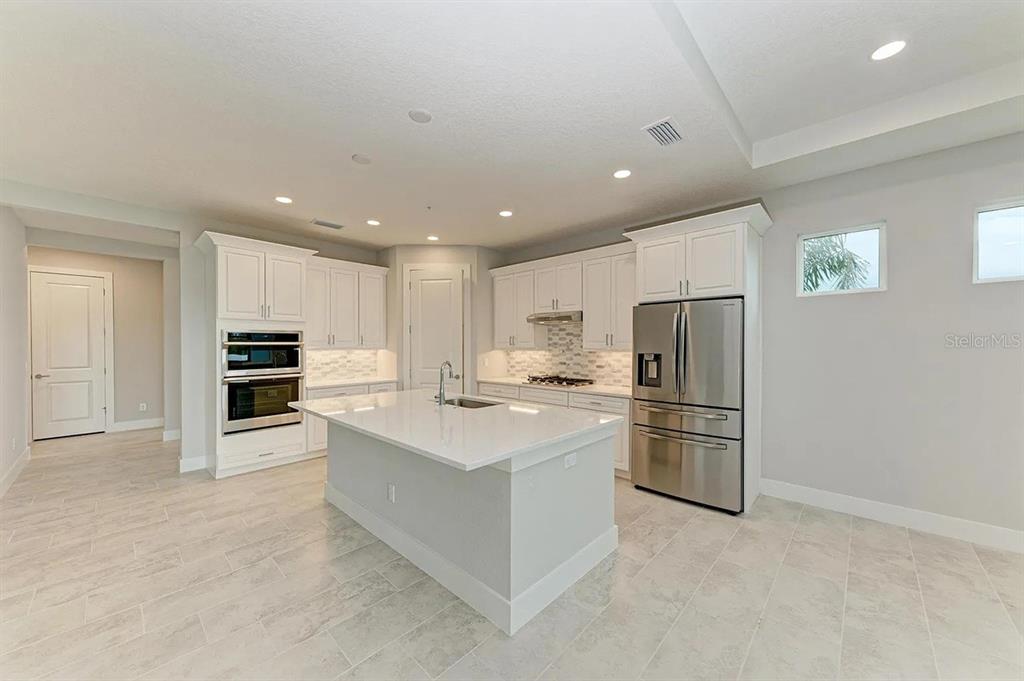 A modern kitchen features white cabinetry, a central island, stainless steel appliances, and tiled flooring — 10016 REMBRANDT WAY UNIT 102, BRADENTON, FL