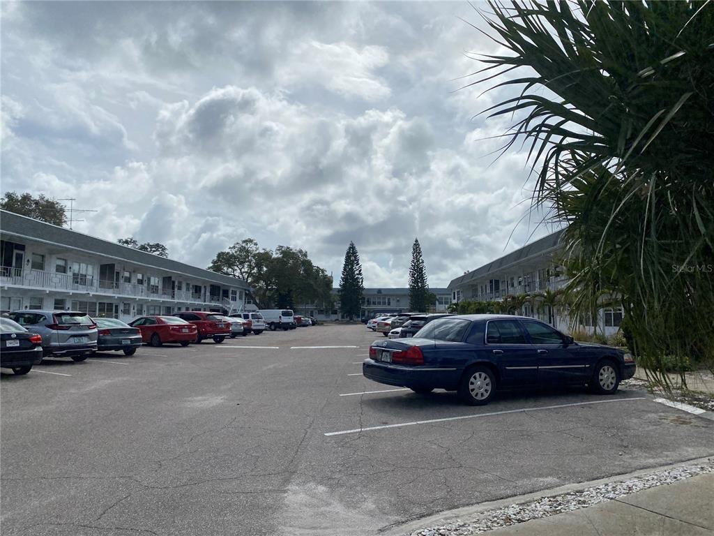A parking lot sits between two multi-story apartment buildings under a cloudy sky — 1221 DREW STREET UNIT A17, CLEARWATER, FL