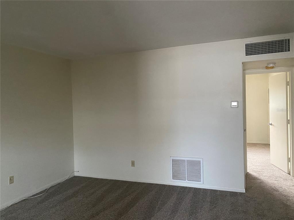 An empty room with beige carpet, white walls, a floor vent, and an open doorway — 1221 DREW STREET UNIT A17, CLEARWATER, FL