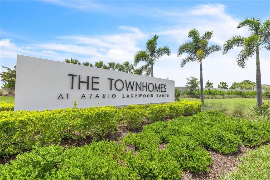 A white sign for The Townhomes at Azario Lakewood Ranch stands in a landscaped area — 16632 BERGAMO PLACE, BRADENTON, FL