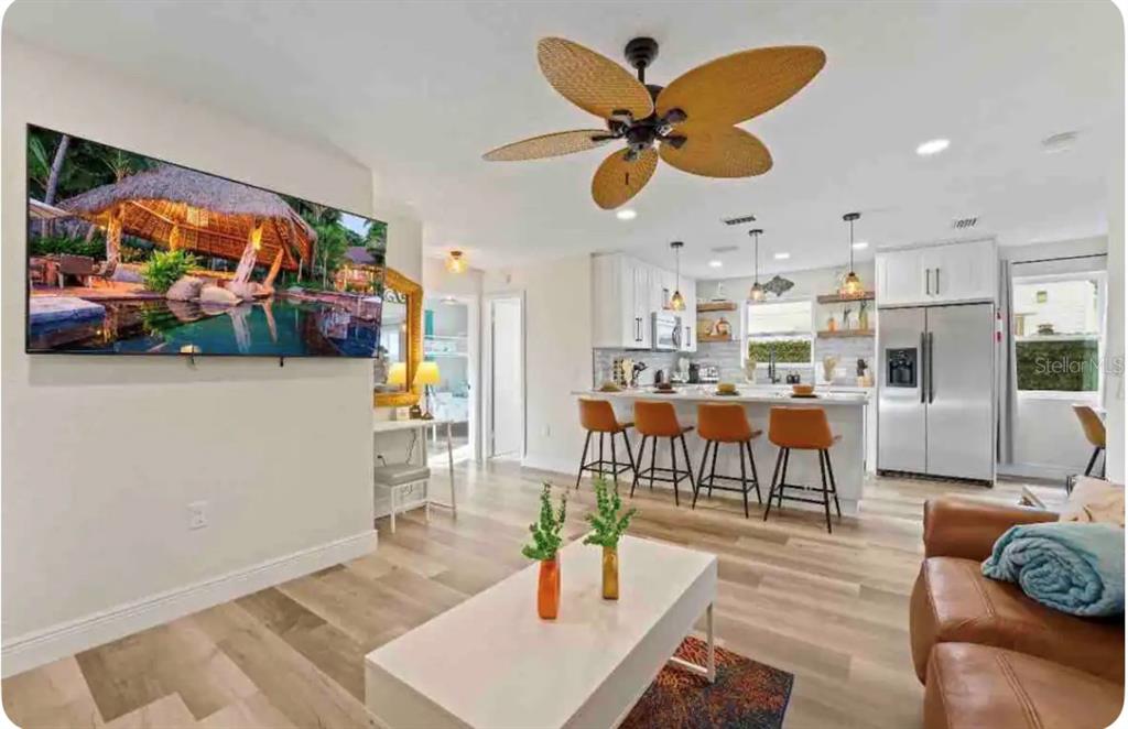 An open-concept living room and kitchen featuring a ceiling fan, island seating, and wood flooring — 301 N HOLLYWOOD AVENUE, DAYTONA BEACH, FL