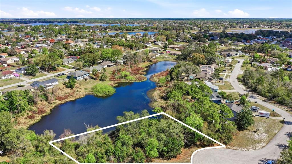 An aerial view shows a vacant, wooded lot bordering a pond in a residential neighborhood — 2328 BRIMHALL COURT, DELTONA, FL