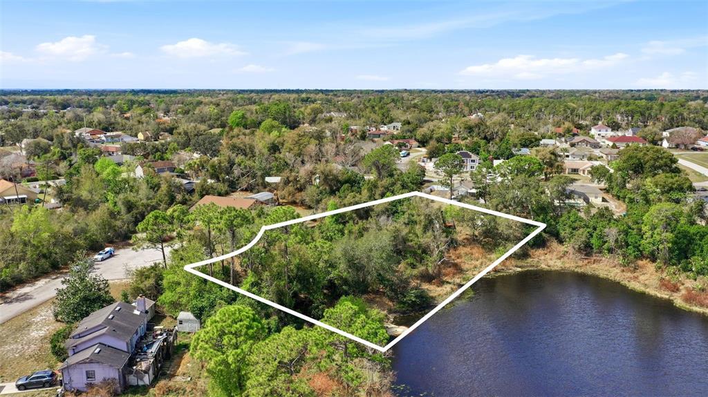 An aerial view shows a vacant, tree-covered lot outlined in white next to a lake — 2328 BRIMHALL COURT, DELTONA, FL