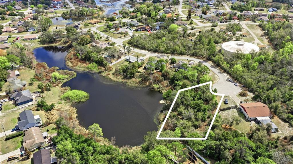 An aerial view shows a vacant, wooded lot outlined in white next to a lake — 2328 BRIMHALL COURT, DELTONA, FL