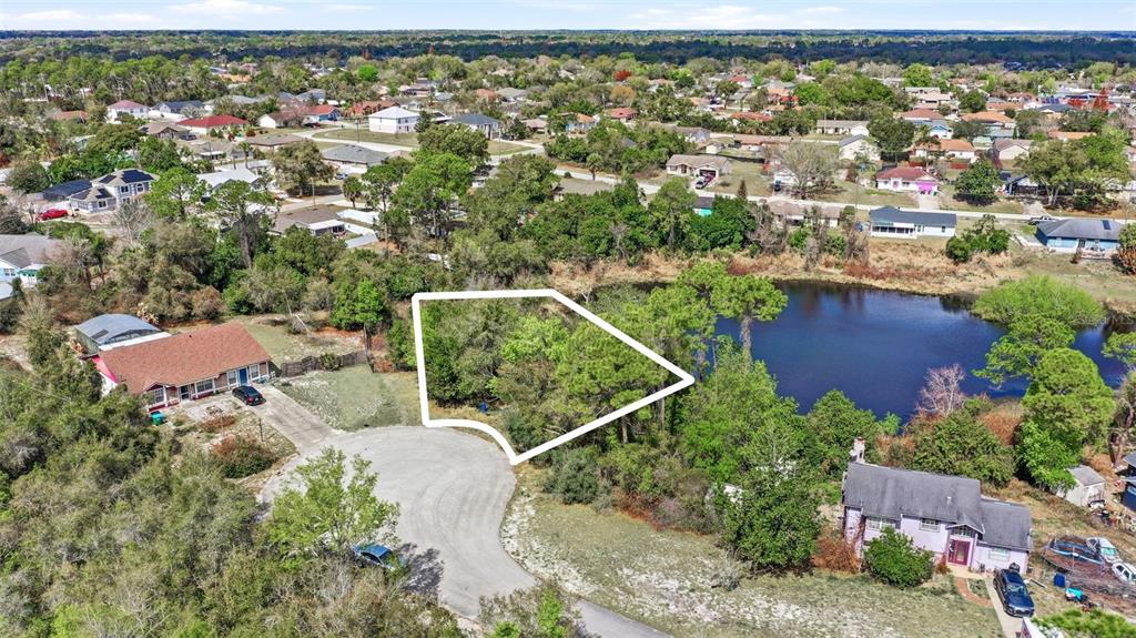 An aerial view shows a vacant, wooded lot outlined in white next to a pond — 2328 BRIMHALL COURT, DELTONA, FL