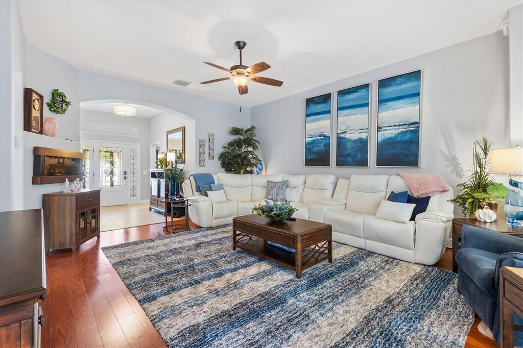 A living room features a white sectional sofa, a blue striped rug, and wall art — 562 BRADFORD LOOP, THE VILLAGES, FL