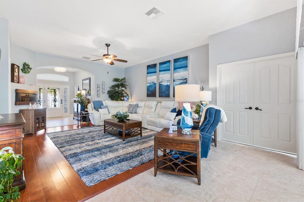 A living room features a white sectional sofa, blue area rug, and wood flooring — 562 BRADFORD LOOP, THE VILLAGES, FL