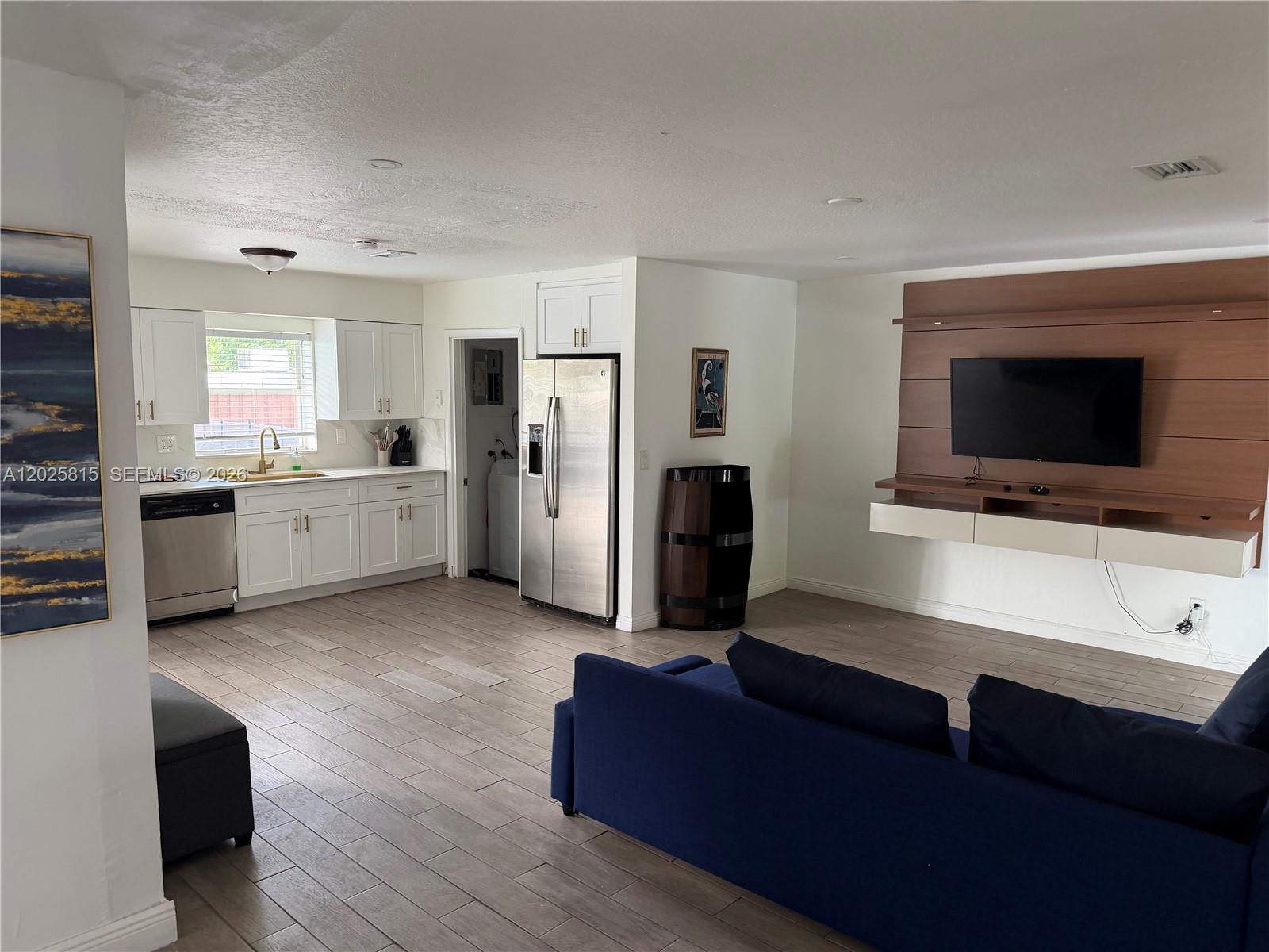 An open-concept living area features a white kitchen, stainless steel appliances, and a wall-mounted television — 19640 Lenaire Dr, Cutler Bay FL 33157, CUTLER BAY, FL