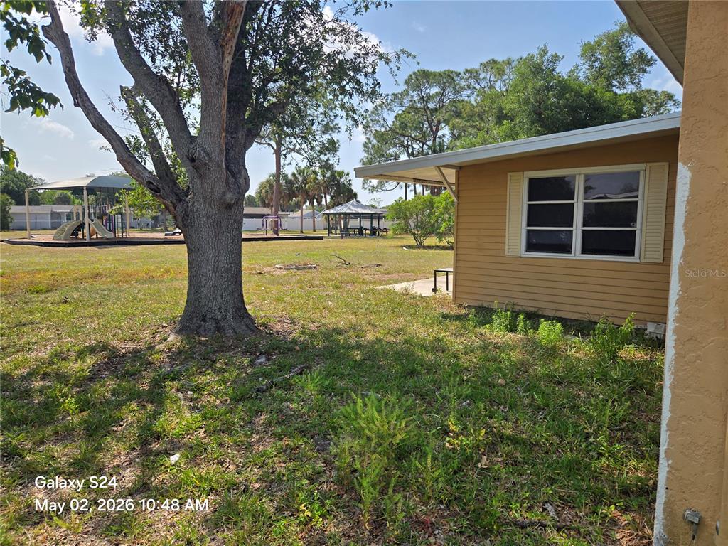 A view of a grassy yard next to a tan house with a playground nearby — 3322 BOHIO STREET, NORTH PORT, FL