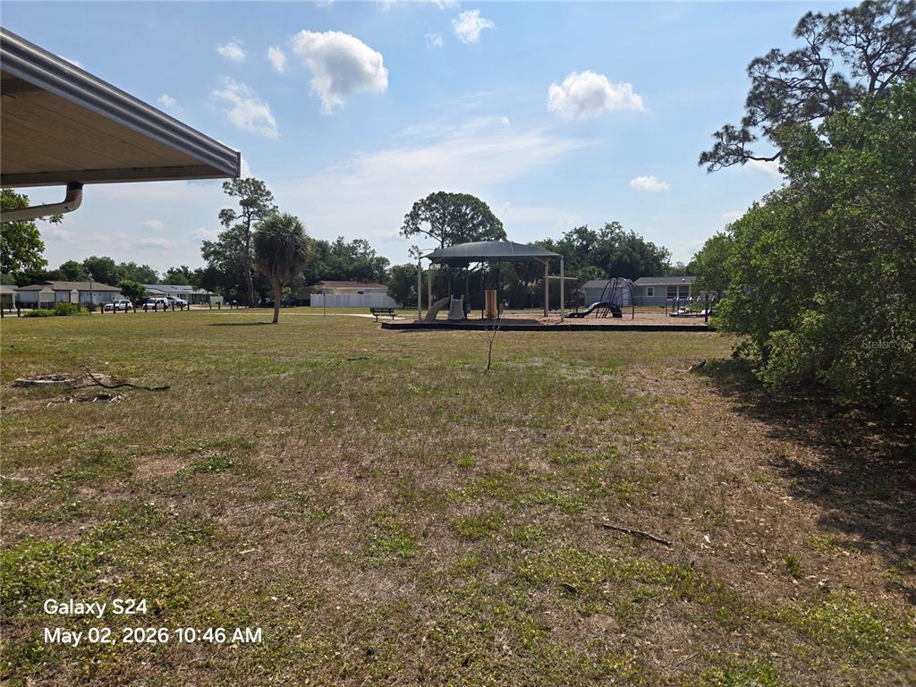 A grassy backyard features a covered playground structure under a bright, partly cloudy sky — 3322 BOHIO STREET, NORTH PORT, FL