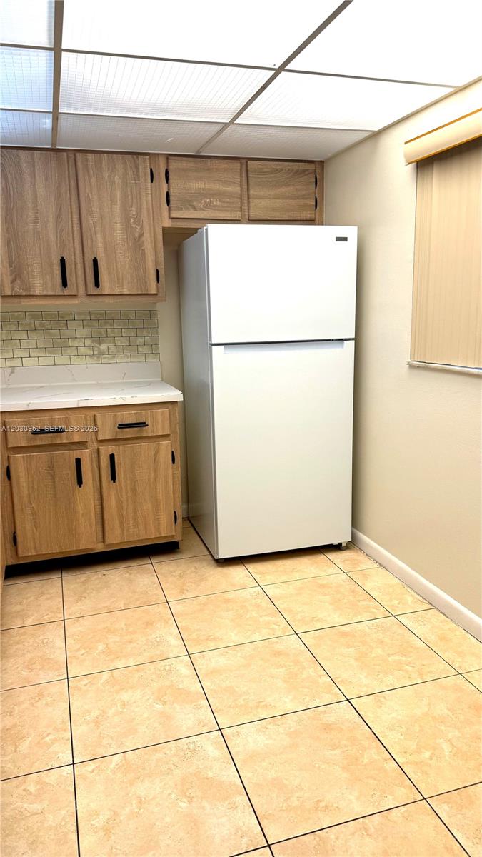 A kitchen features wood-look cabinets, a white refrigerator, a tiled backsplash, and light-colored floor tiles — 8540 SW 133rd Ave Rd # 422, Miami FL 33183, MIAMI, FL