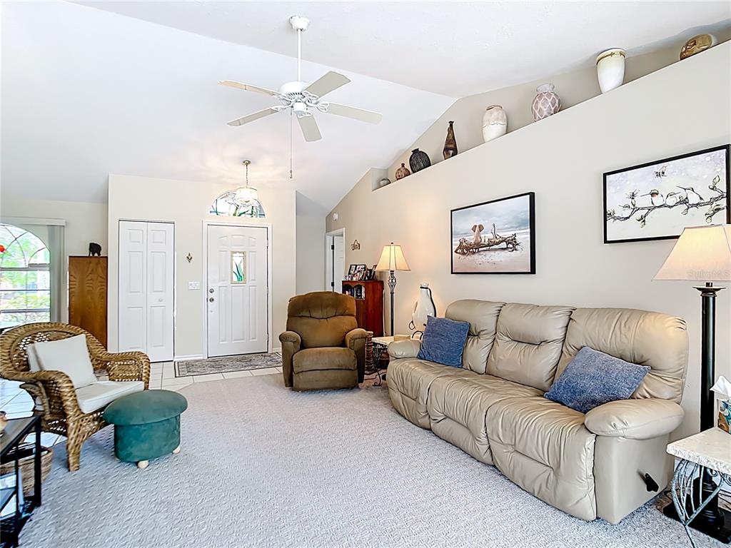 A living room features a vaulted ceiling, beige carpet, a tan sofa, and a wicker chair — 4812 ALFA TERRACE, NORTH PORT, FL