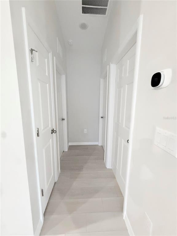 A narrow hallway features light-colored tile flooring, white doors, and a wall-mounted smart thermostat — 12163 CATTLESIDE DRIVE, RIVERVIEW, FL