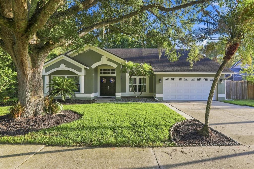 A single-story house with green stucco siding, a two-car garage, and a large front tree — 2200 EKANA DRIVE, OVIEDO, FL