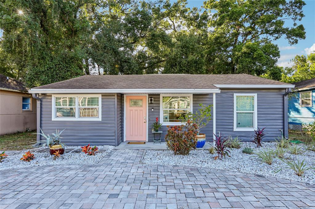 A single-story house with gray horizontal siding, a pink front door, and a paver driveway — 4104 N SEMINOLE AVENUE, TAMPA, FL
