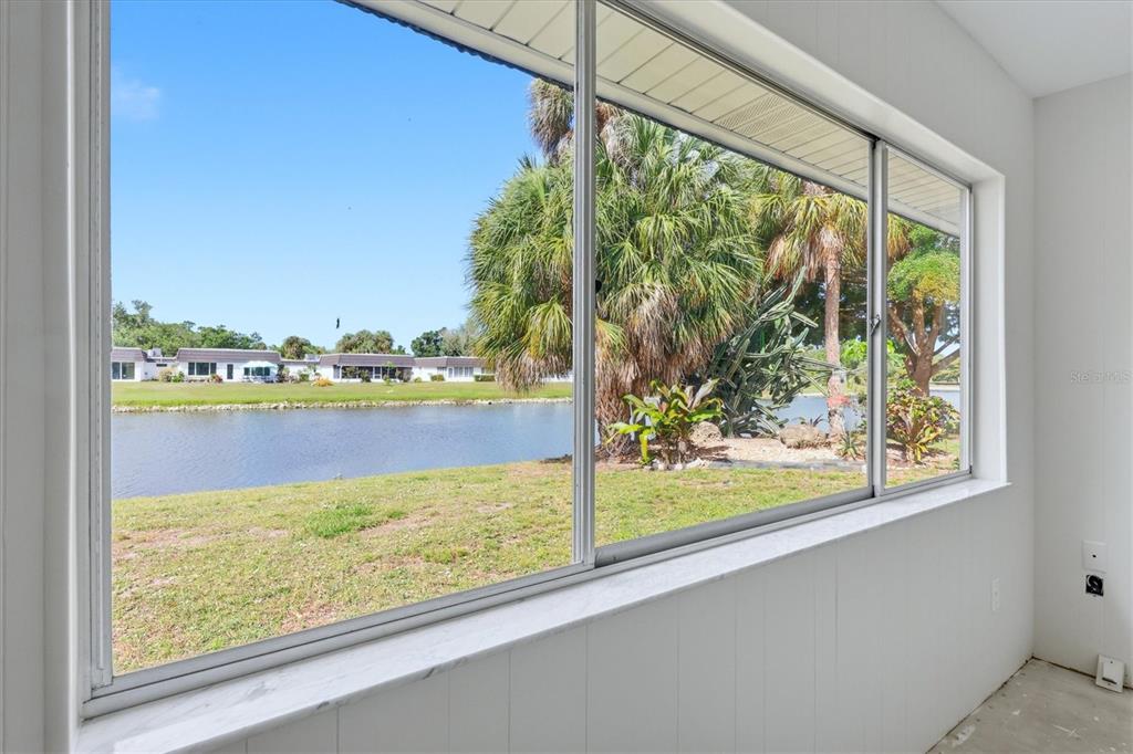 A sunroom with white paneled walls overlooks a lake and palm trees through large windows — 3960 LAKESIDE ROAD UNIT 156, SARASOTA, FL