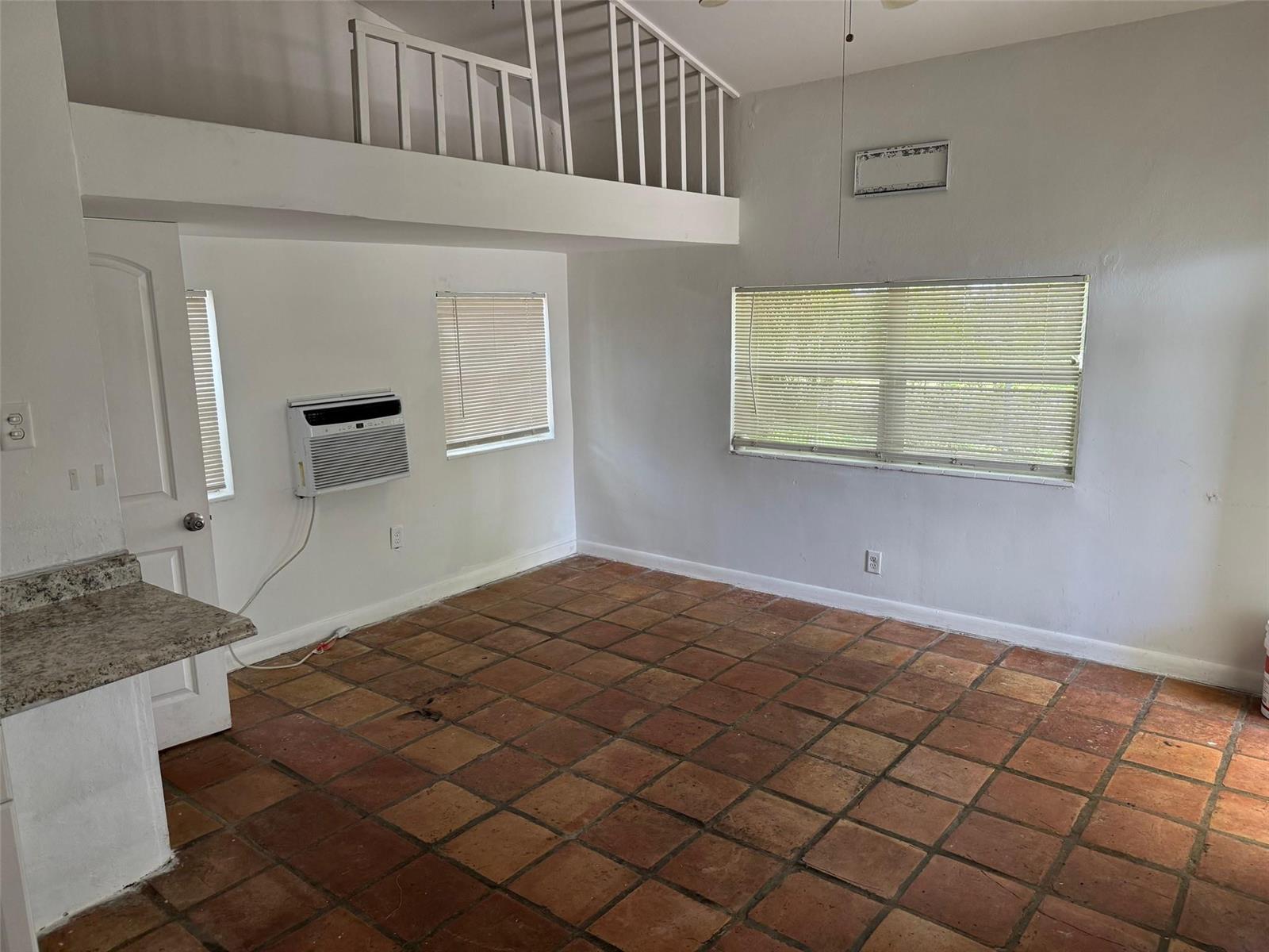A room with terracotta tile flooring, a loft area with railings, and a window air conditioner — 8261 NW 1st Place # 3, Miami FL 33150, MIAMI, FL