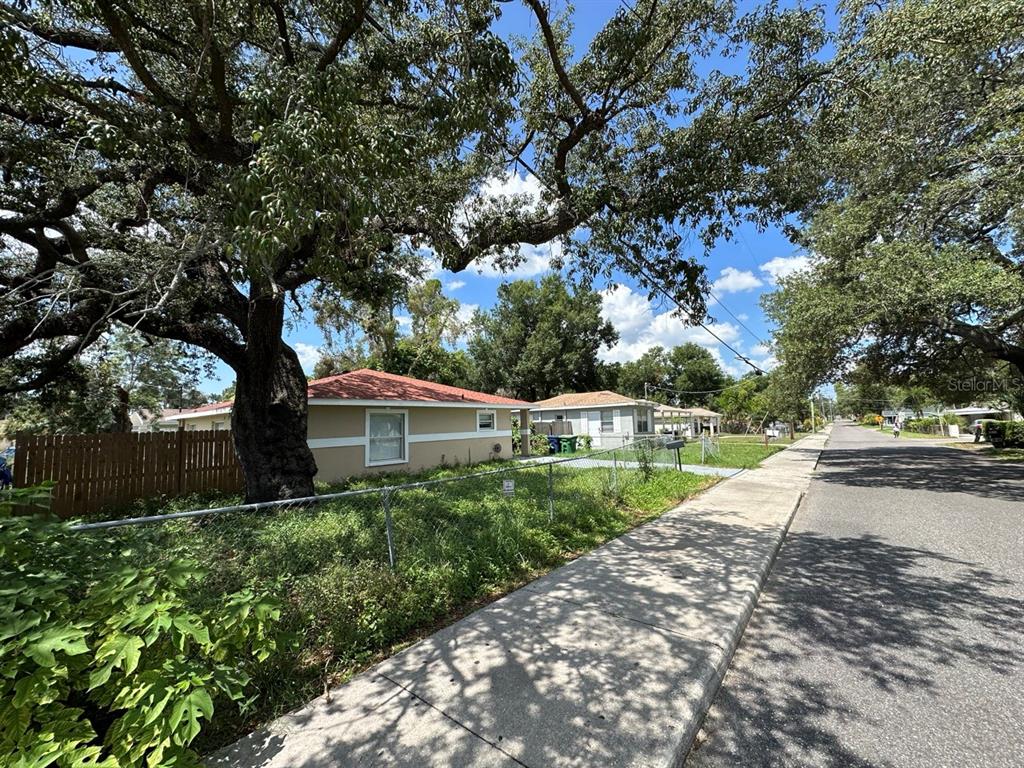 A single-story house with a red roof sits behind a chain-link fence and large trees — 3613 E CHELSEA STREET, TAMPA, FL