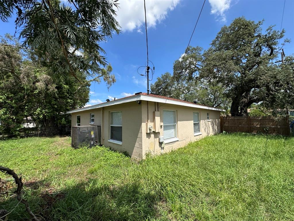 The exterior of a tan, single-story house with a flat roof and overgrown grass — 3613 E CHELSEA STREET, TAMPA, FL