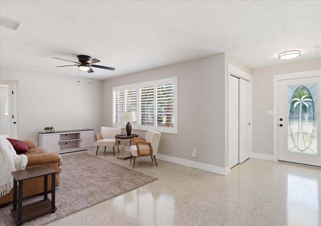 A living room features light-colored walls, a ceiling fan, plantation shutters, and polished terrazzo flooring — 3014 58TH STREET S, GULFPORT, FL