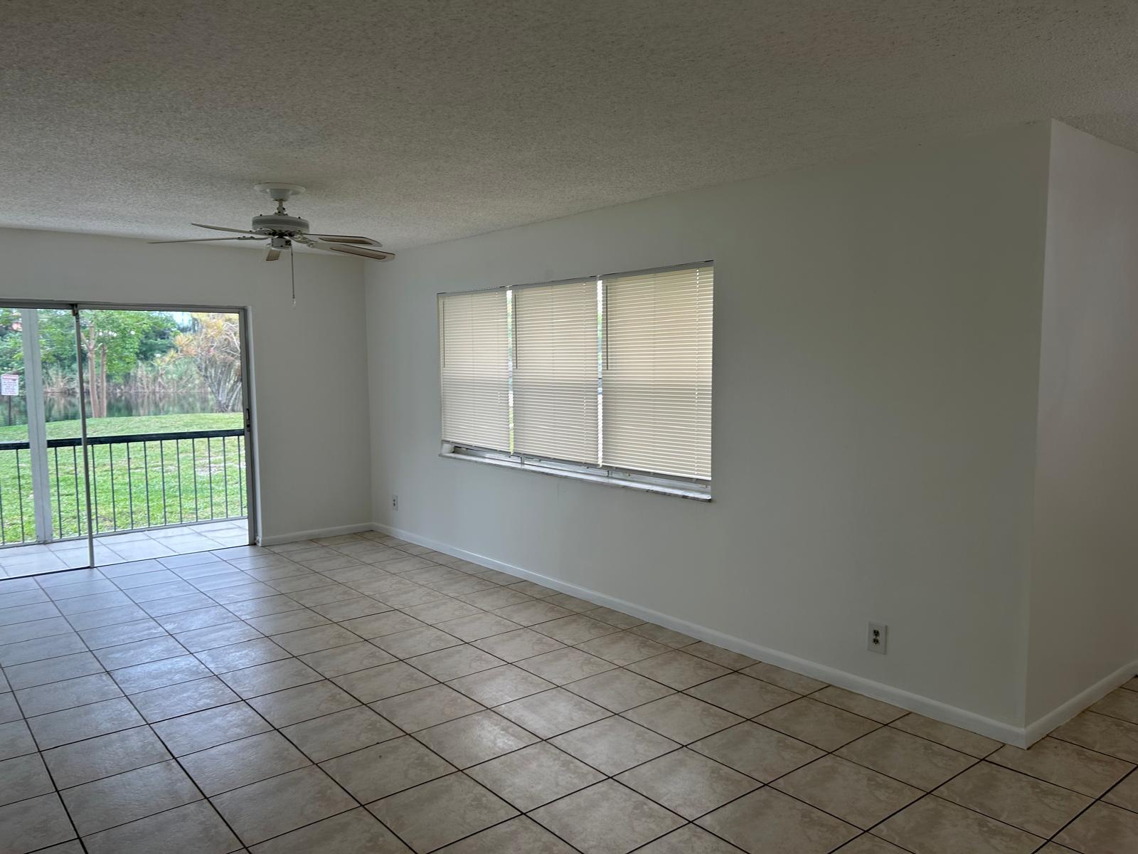 An empty room features tile flooring, a ceiling fan, large windows, and a sliding door — 3300 Spanish Moss Terrace, Lauderhill FL 33319, LAUDERHILL, FL