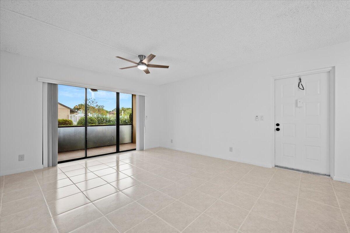 An empty living room features white walls, light tile flooring, a ceiling fan, and sliding doors — 708 Sunny Pine Way # B1, FL 33415, FL