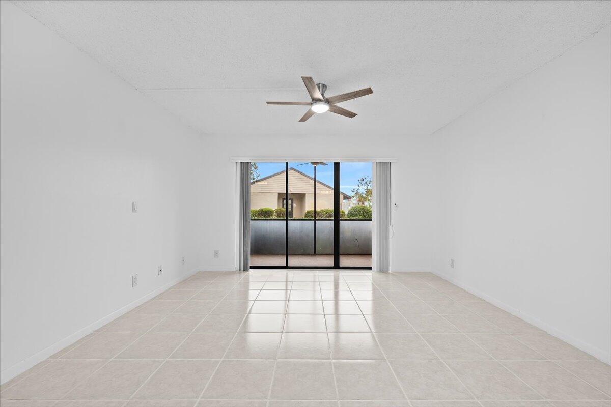 A bright, empty room with white walls, tile flooring, a ceiling fan, and sliding doors — 708 Sunny Pine Way # B1, FL 33415, FL