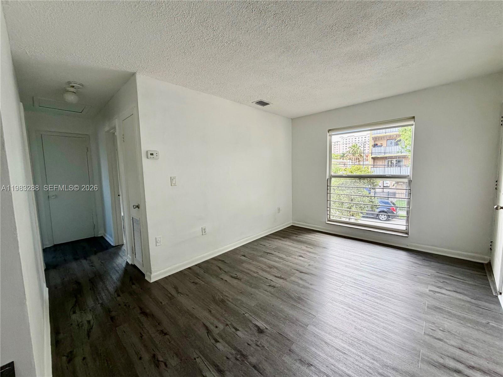 An empty room features white walls, wood-look flooring, and a window with metal security bars — 1305 NW 4th St # 3, Miami FL 33125, MIAMI, FL