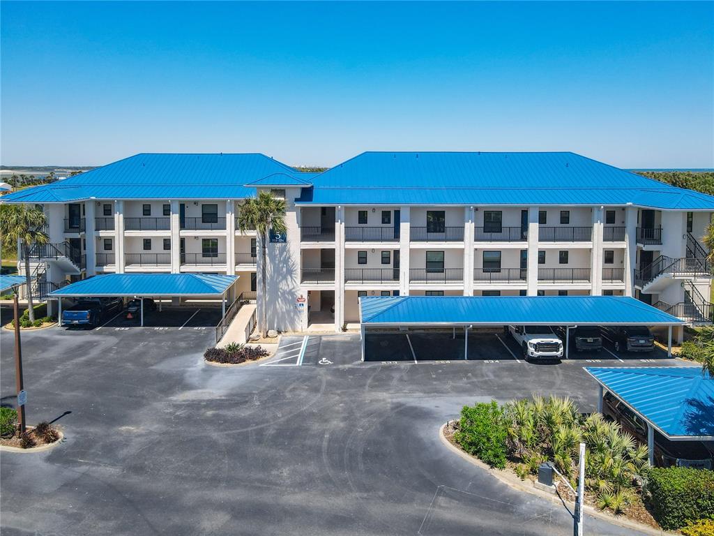 An aerial view shows a multi-story building with a blue roof, parking lot, and tennis court — 2700 N PENINSULA AVENUE UNIT 536, NEW SMYRNA BEACH, FL