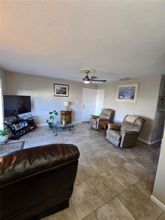 A living room with tile flooring, a ceiling fan, two leather recliners, and a television — 5231 BEACH DRIVE SE UNIT A, ST PETERSBURG, FL