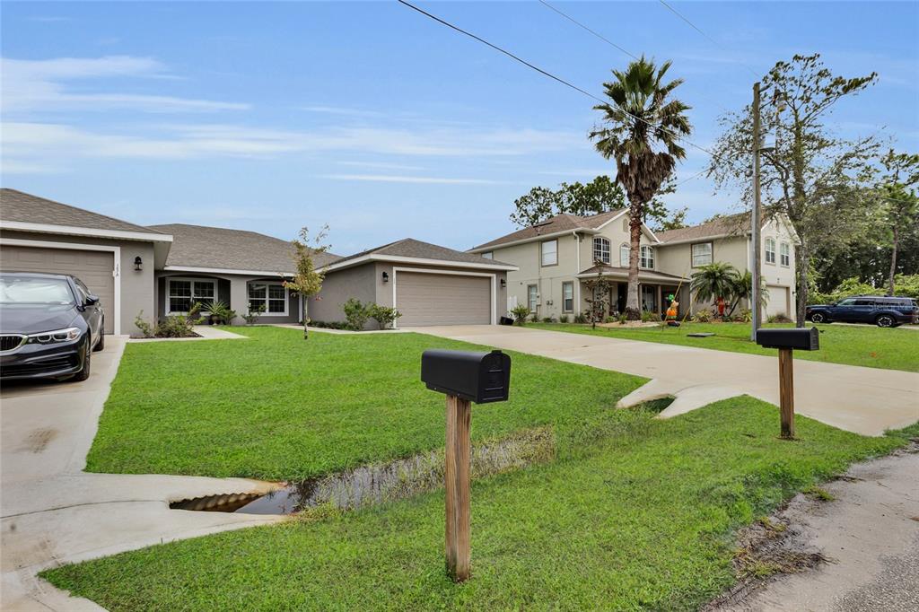 A view of two suburban houses with attached garages, front lawns, and mailboxes along a street — 13 LLOVERA  PLACE, PALM COAST, FL
