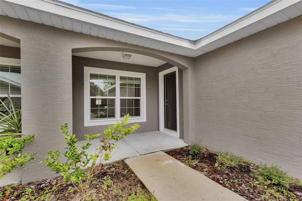 A concrete walkway leads to the covered entryway of a house with gray stucco walls — 13 LLOVERA  PLACE, PALM COAST, FL