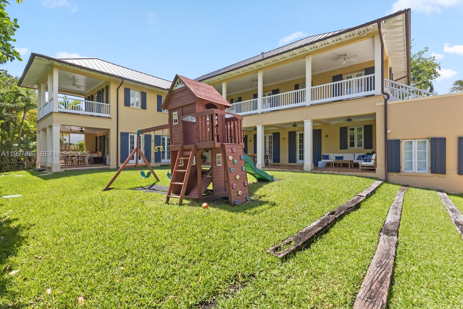 The exterior of a two-story yellow house features a wooden playset in the backyard — 685 Harbor Ln, Key Biscayne FL 33149, KEY BISCAYNE, FL