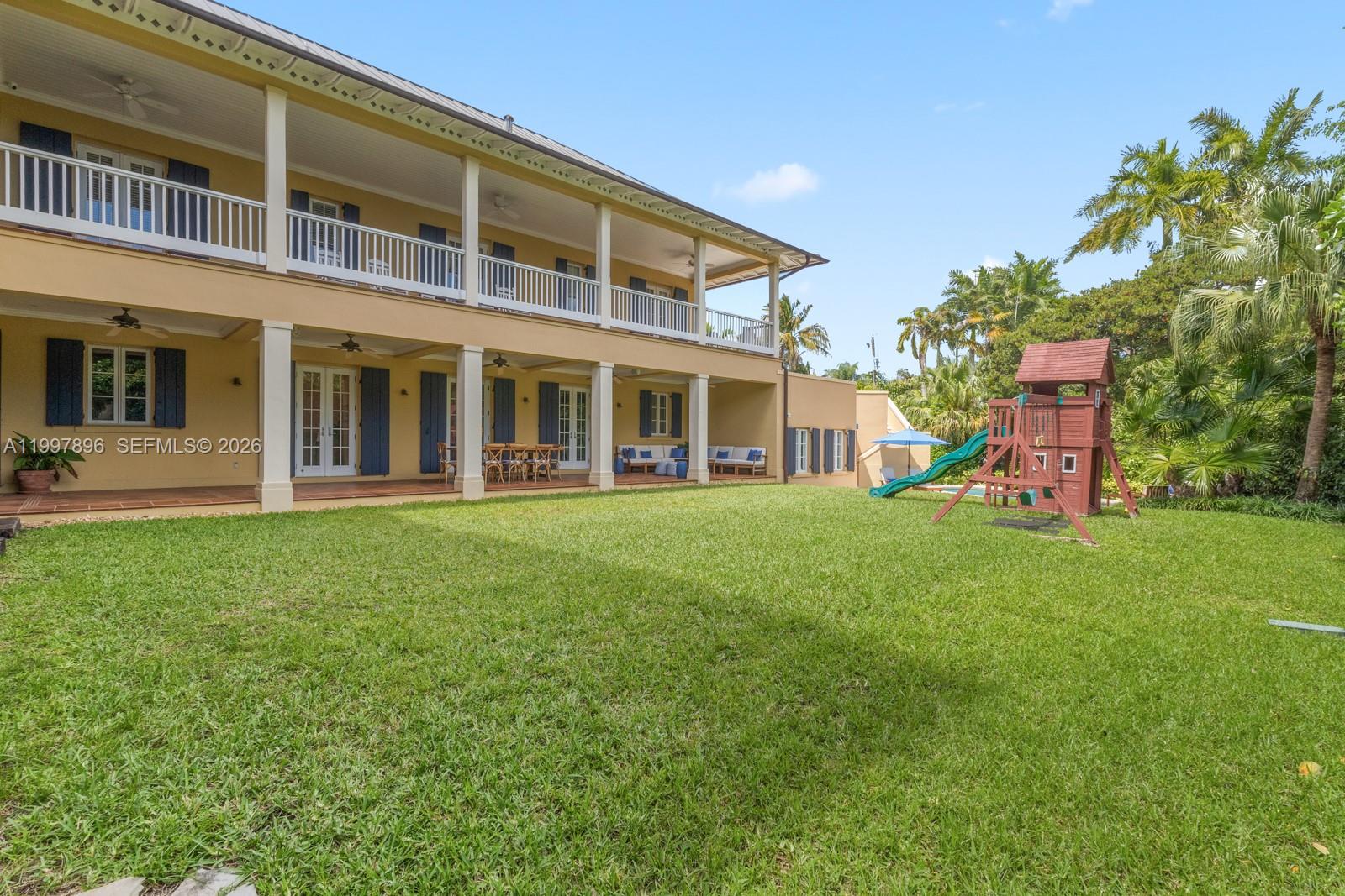 The exterior of a two-story yellow house features a large grassy lawn and a playground — 685 Harbor Ln, Key Biscayne FL 33149, KEY BISCAYNE, FL