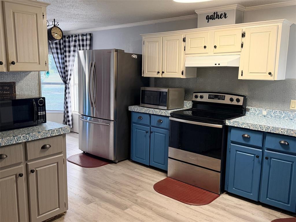 A kitchen features blue lower cabinets, cream upper cabinets, stainless steel appliances, and patterned countertops — 14790 NW 72ND COURT, CHIEFLAND, FL