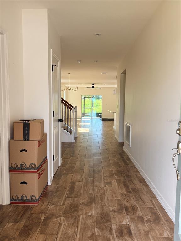 A hallway with wood-look tile flooring leads toward a staircase and a bright living area — 1212 CANFIELD CIRCLE SE, PALM BAY, FL