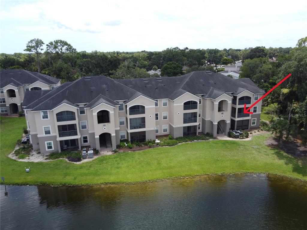 An aerial view of a multi-story apartment building situated next to a pond — 940 VILLAGE TRAIL UNIT 4-202, PORT ORANGE, FL