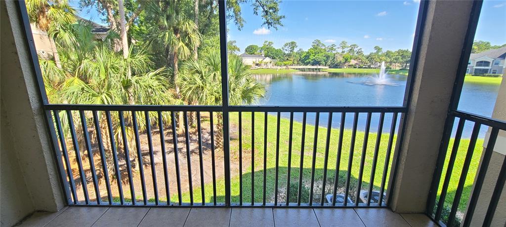 A screened-in balcony overlooks a lake with a fountain and surrounding palm trees — 940 VILLAGE TRAIL UNIT 4-202, PORT ORANGE, FL
