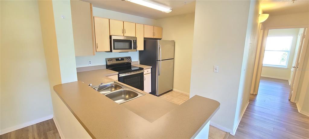 A kitchen with light wood cabinets, stainless steel appliances, and a peninsula countertop — 940 VILLAGE TRAIL UNIT 4-202, PORT ORANGE, FL