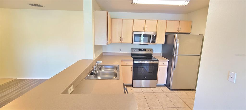 A kitchen features light wood cabinets, stainless steel appliances, and a double-basin sink — 940 VILLAGE TRAIL UNIT 4-202, PORT ORANGE, FL